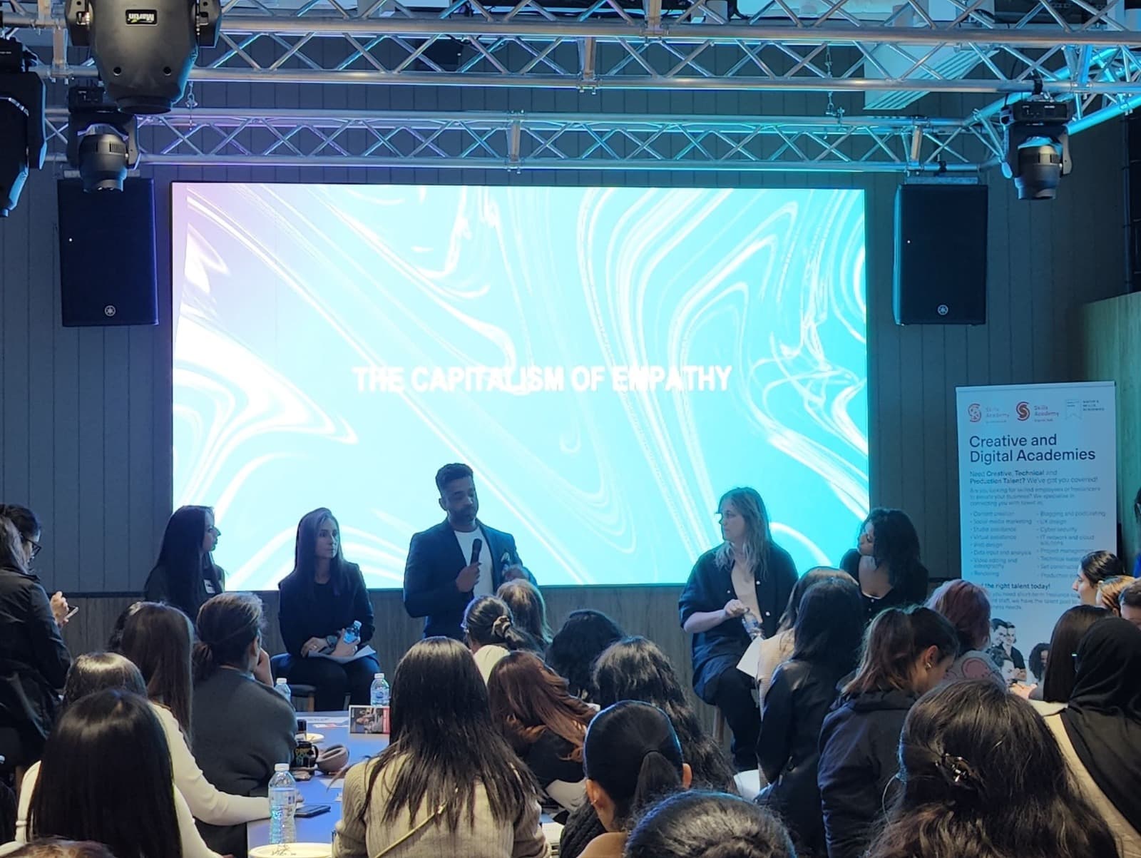 A panel on stage under the title The Capitalism of Empathy.