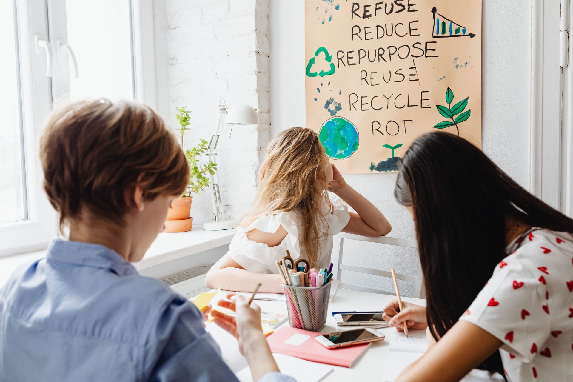 Three teenagers working together on a sustainability poster in a classroom.