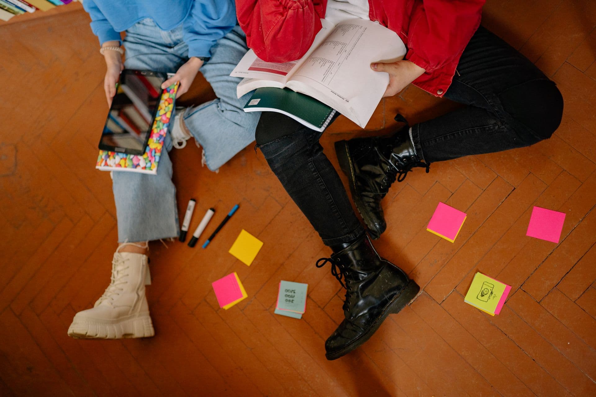 Two students on the floor with books, a tablet and colourful sticky notes.